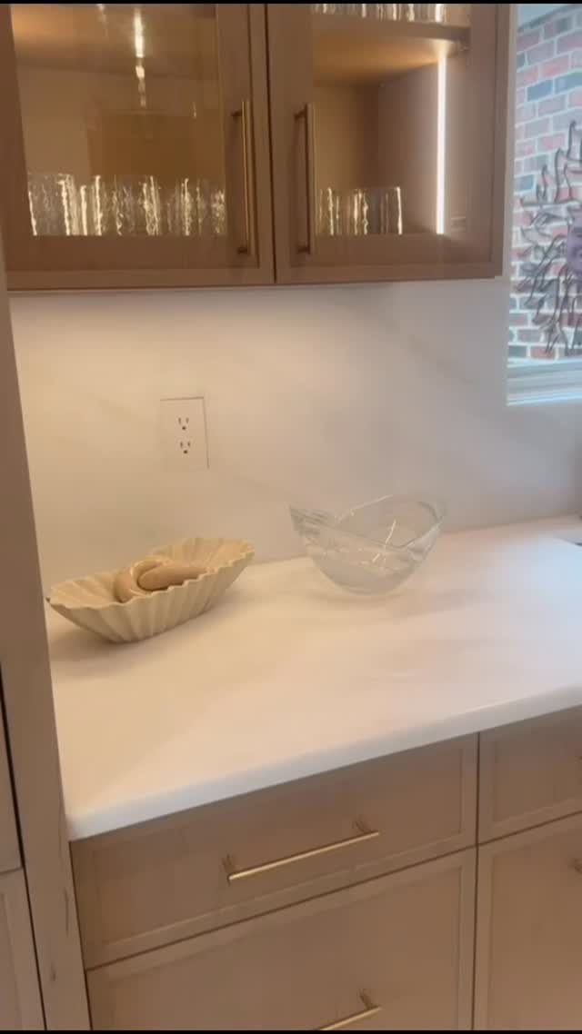 White stone countertop and matching seamless slab backsplash with beige kitchen cabinets.