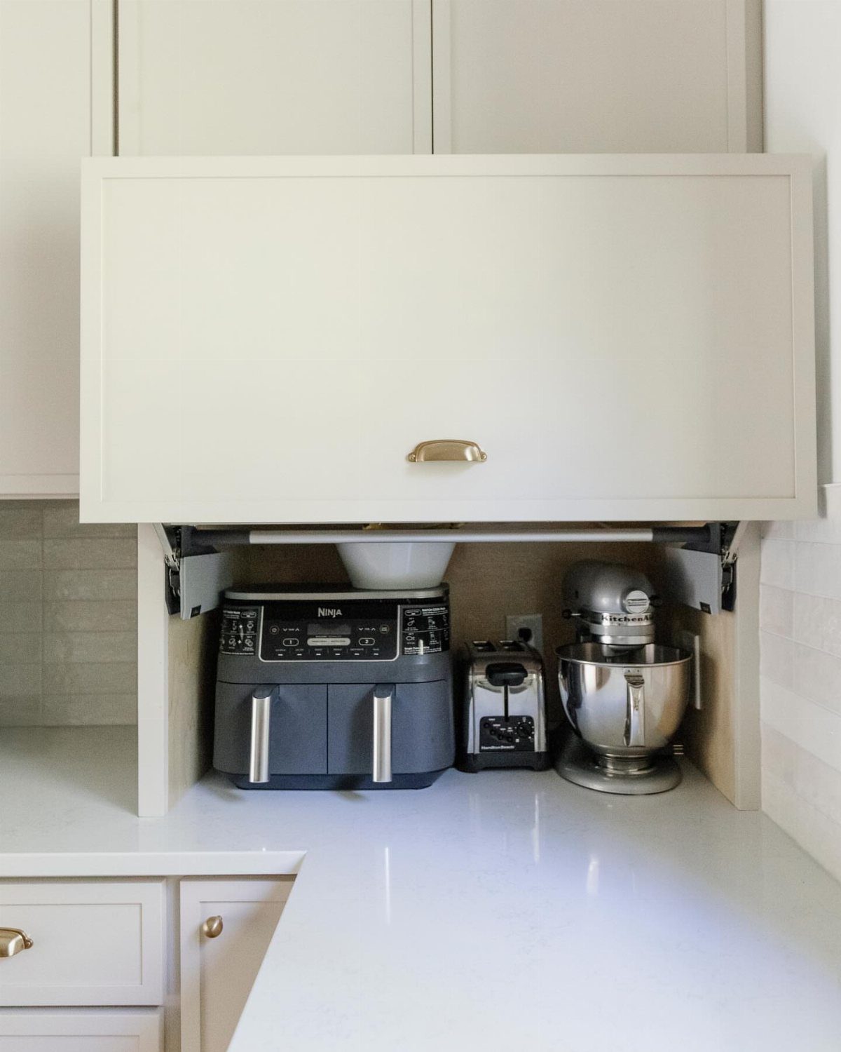 White kitchen cabinet with a lift-up door concealing an air fryer and stand mixer.