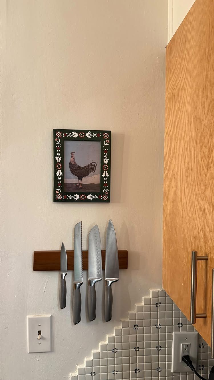 Wooden magnetic knife strip holding four silver knives on a white kitchen wall.