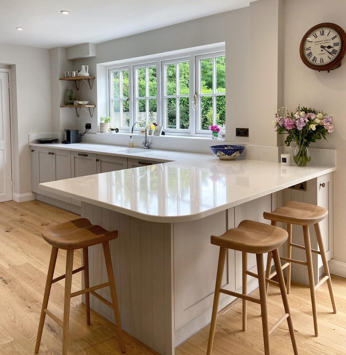 Kitchen peninsula with white quartz countertop and three wooden bar stools in a bright room.