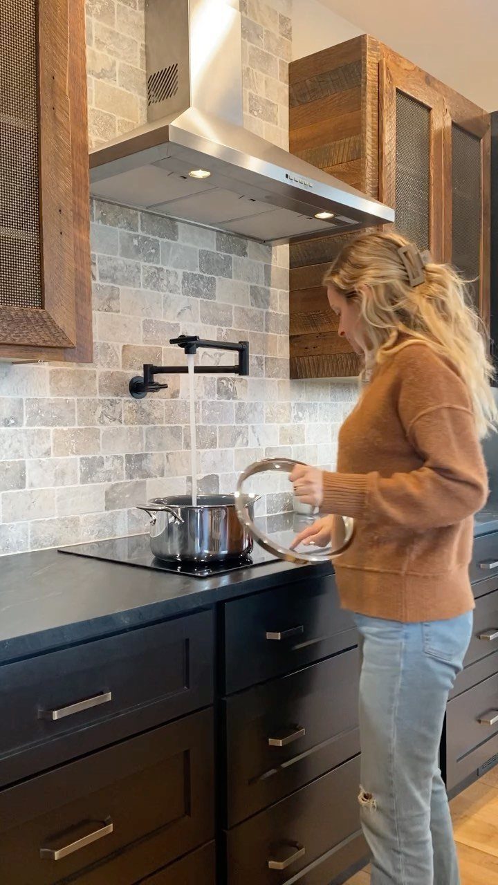 Woman filling a pot on a stove using a black wall-mounted pot filler faucet.