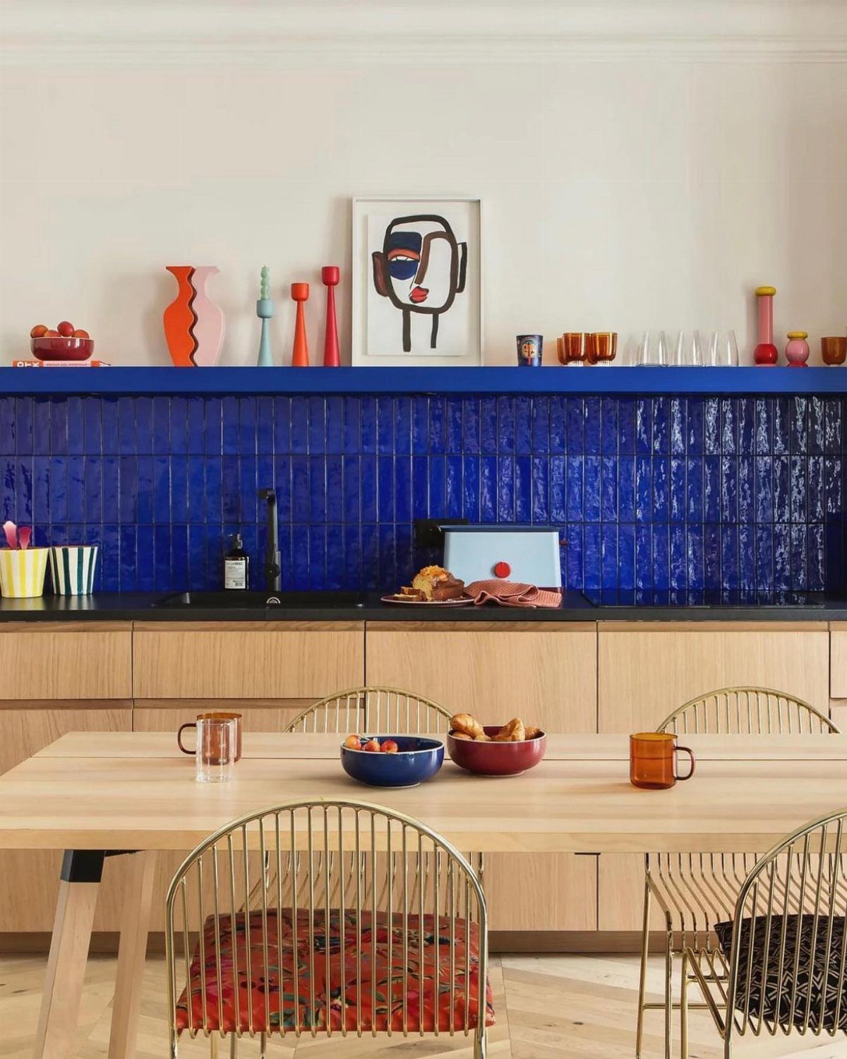 Glossy blue tiled backsplash in a kitchen with light wood cabinets and dining table.
