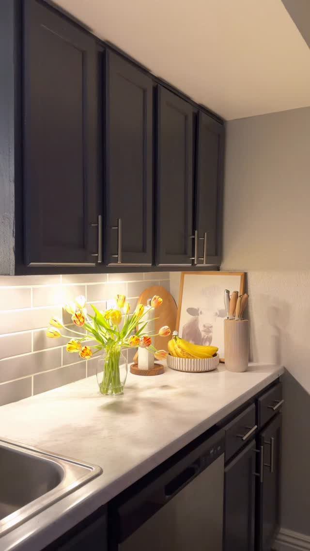 Dark grey kitchen cabinets with warm under-cabinet lighting illuminating yellow tulips on a white counter.