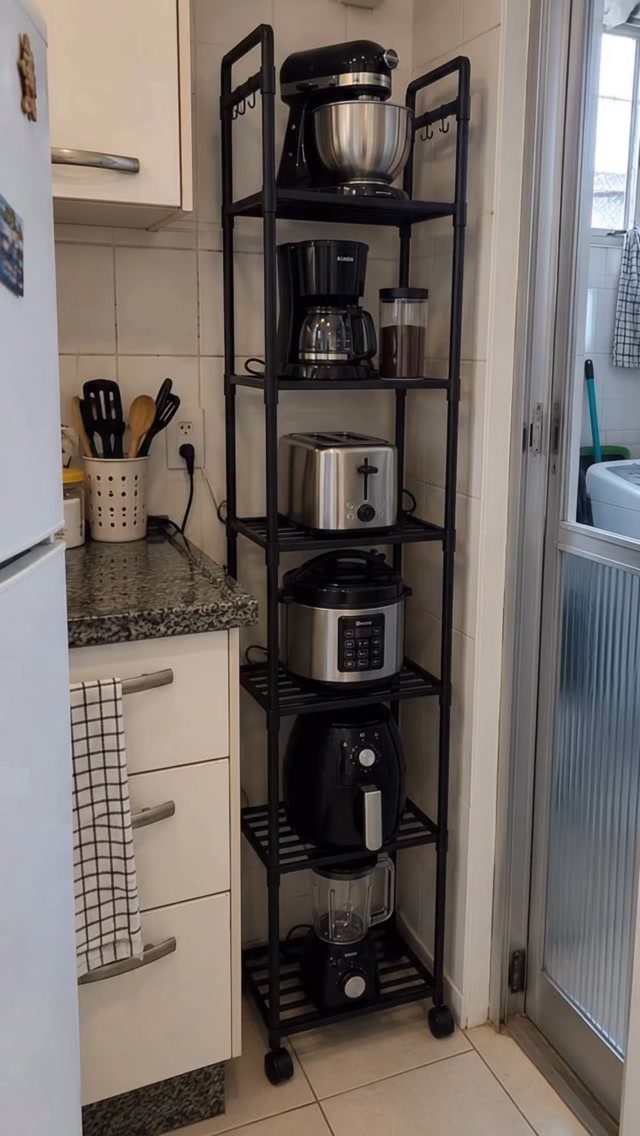 Black metal vertical shelving unit holding various kitchen appliances next to white cabinets.