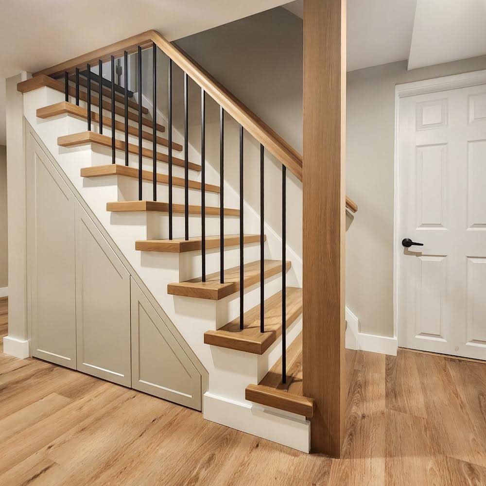 Built-in paneled storage cabinets installed underneath a wooden staircase with black metal spindles.