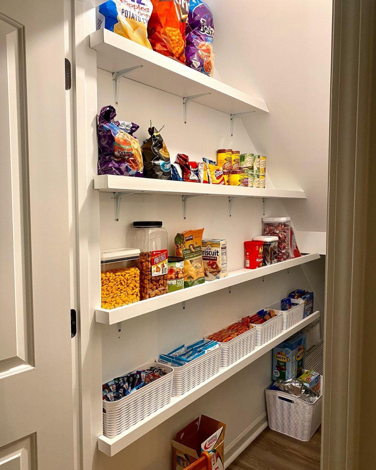 White open shelving in a pantry holding snacks and white woven storage baskets.