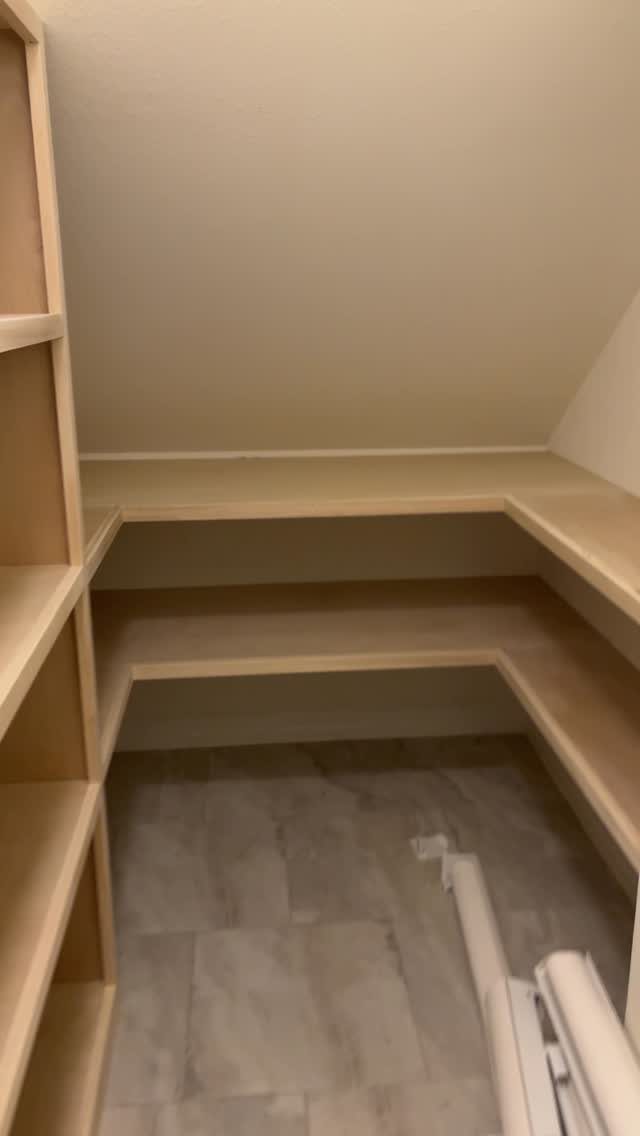 Wooden shelves installed under a sloped ceiling in a small storage area.