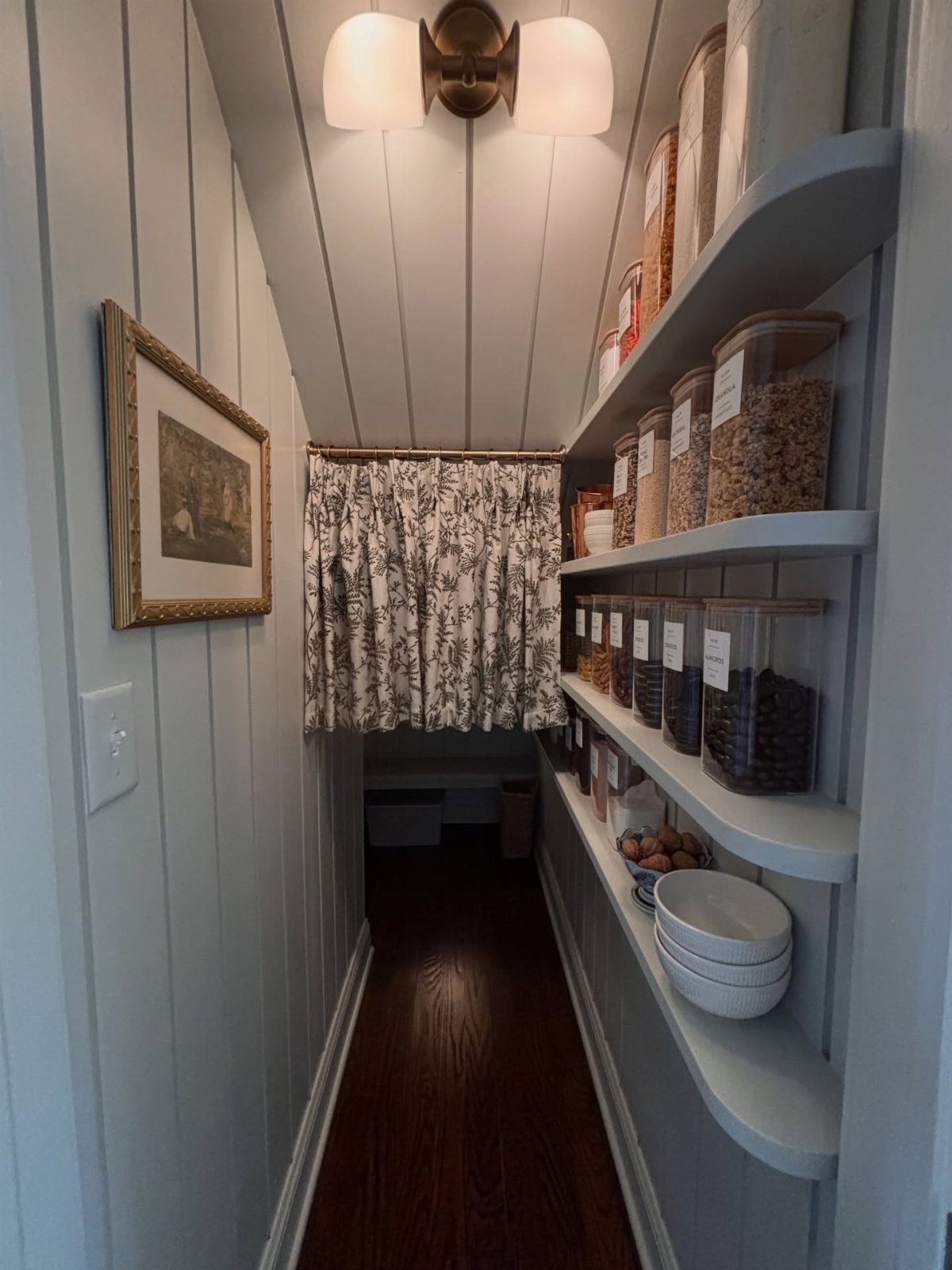 Narrow walk-in pantry with light grey walls and open shelving holding storage jars.