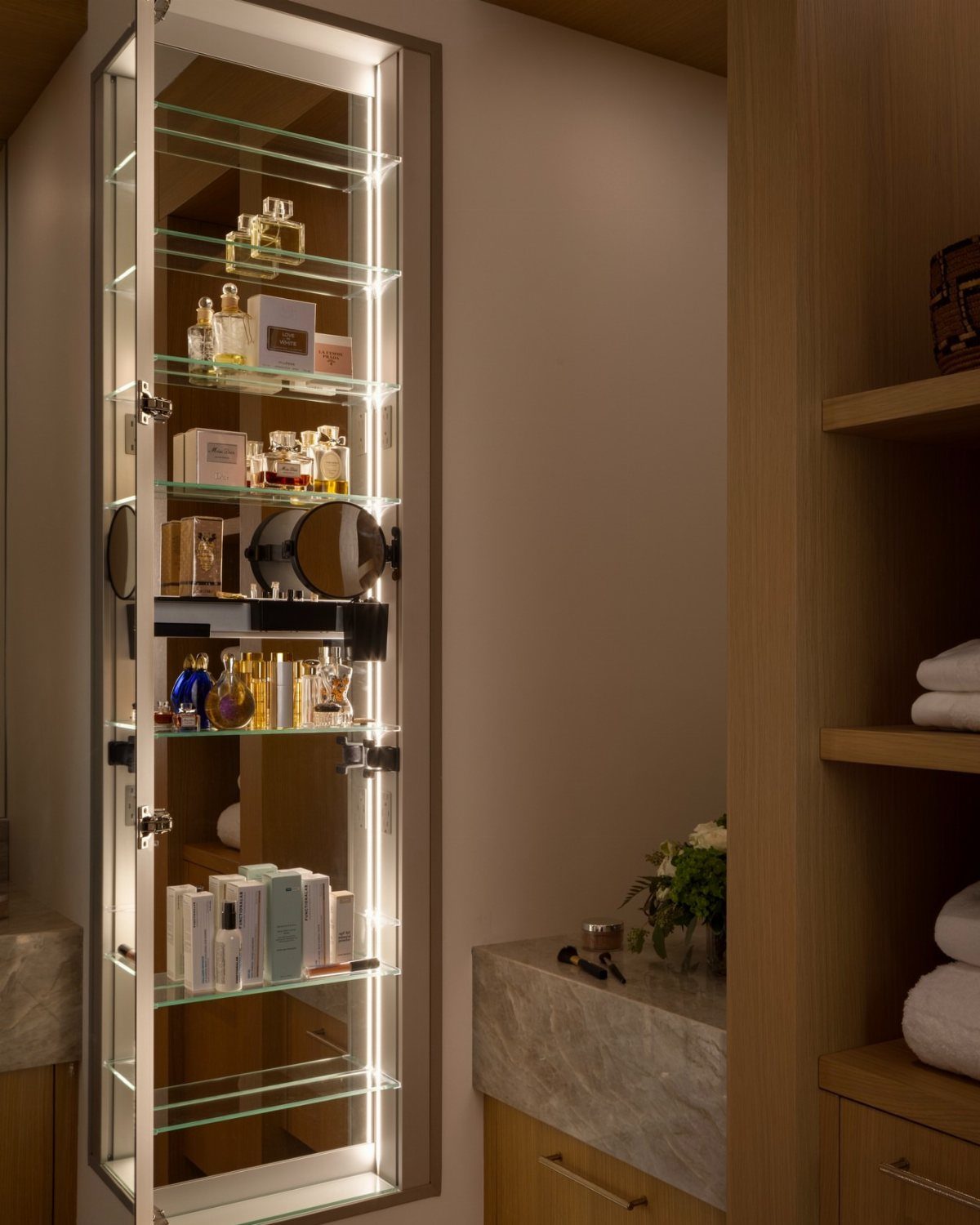 Illuminated bathroom cabinet with glass shelves holding perfumes and skincare products
