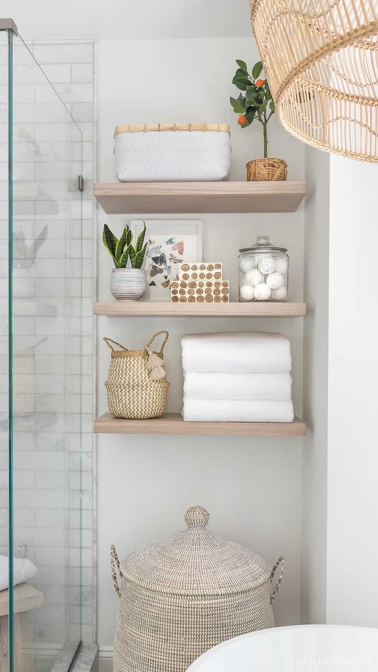 Three light wood floating shelves with towels and baskets on a white bathroom wall.