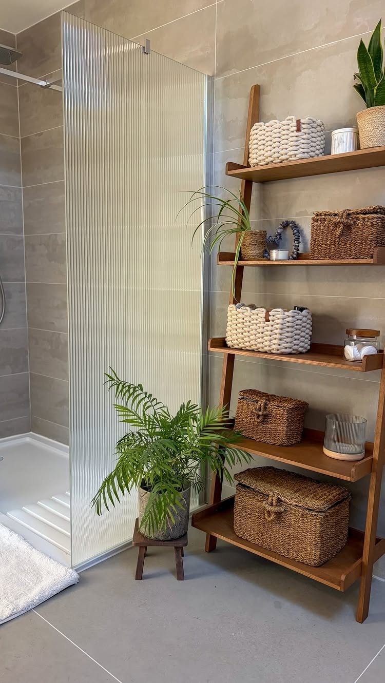 Wooden leaning ladder shelf with woven baskets in a modern grey bathroom.