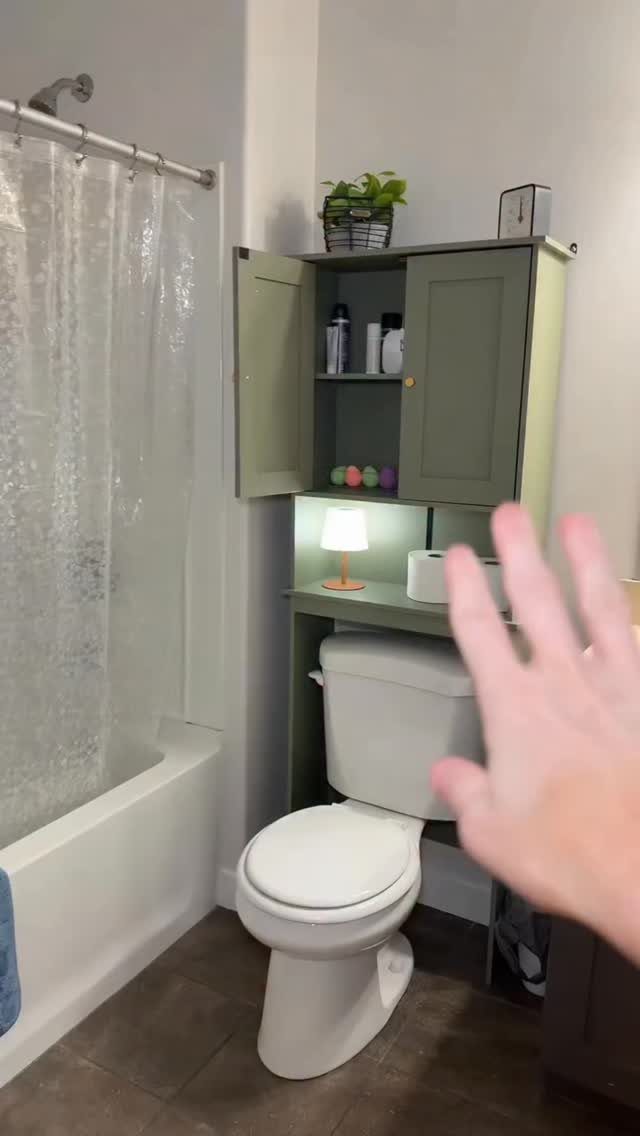 Green storage cabinet with shelves installed over a white toilet in a bathroom