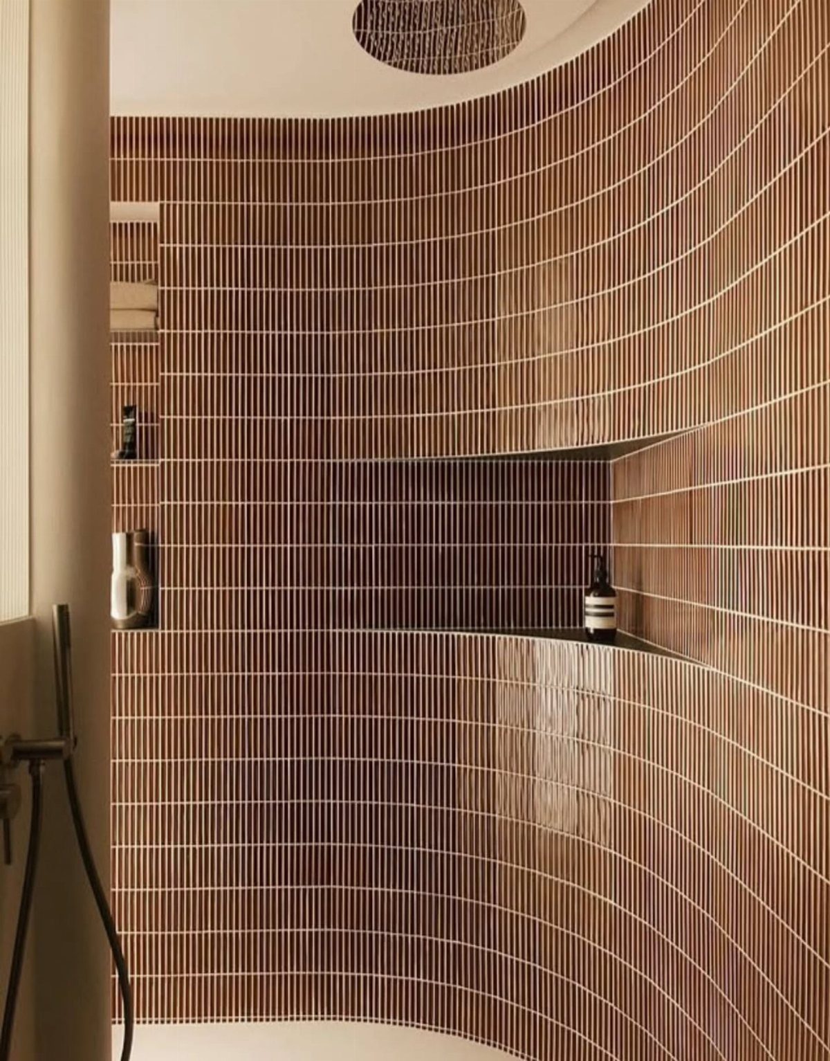 Curved brown tiled bathroom wall with a built-in recessed shower niche shelf.