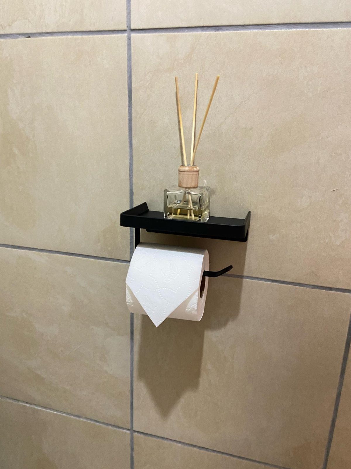 Black wall-mounted bathroom shelf with a fragrance diffuser and toilet paper holder.