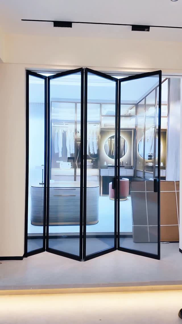 Black-framed bifold glass doors opening into a bright, modern walk-in bedroom closet.