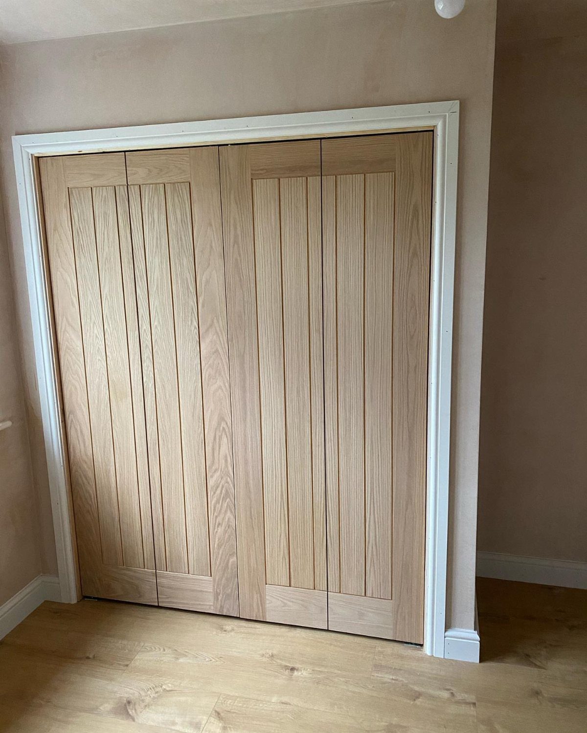 Light wood bifold closet doors with vertical planks and white trim.