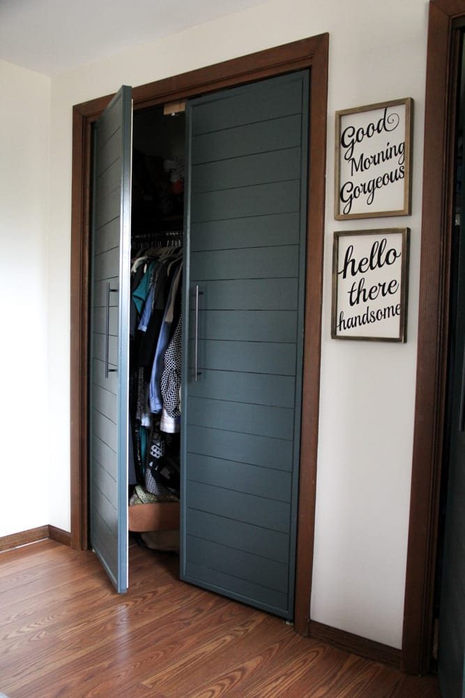 Dark grey shiplap bifold closet doors with long metal handles in a bedroom.
