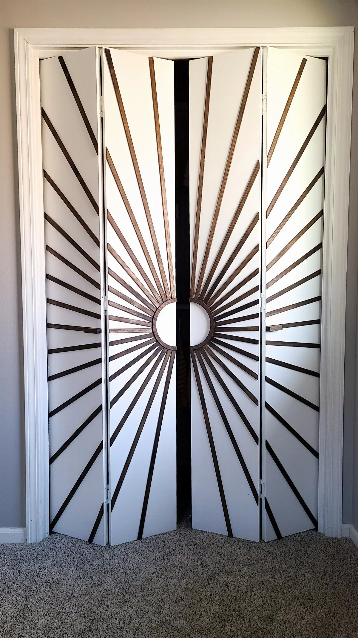 White bifold closet doors with a brown wooden sunburst design radiating from center