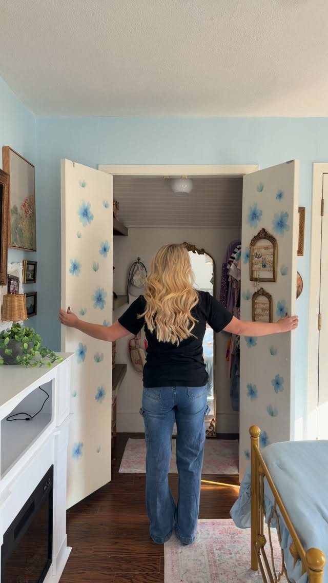 Woman opening white bifold closet doors with blue floral wallpaper patterns in bedroom