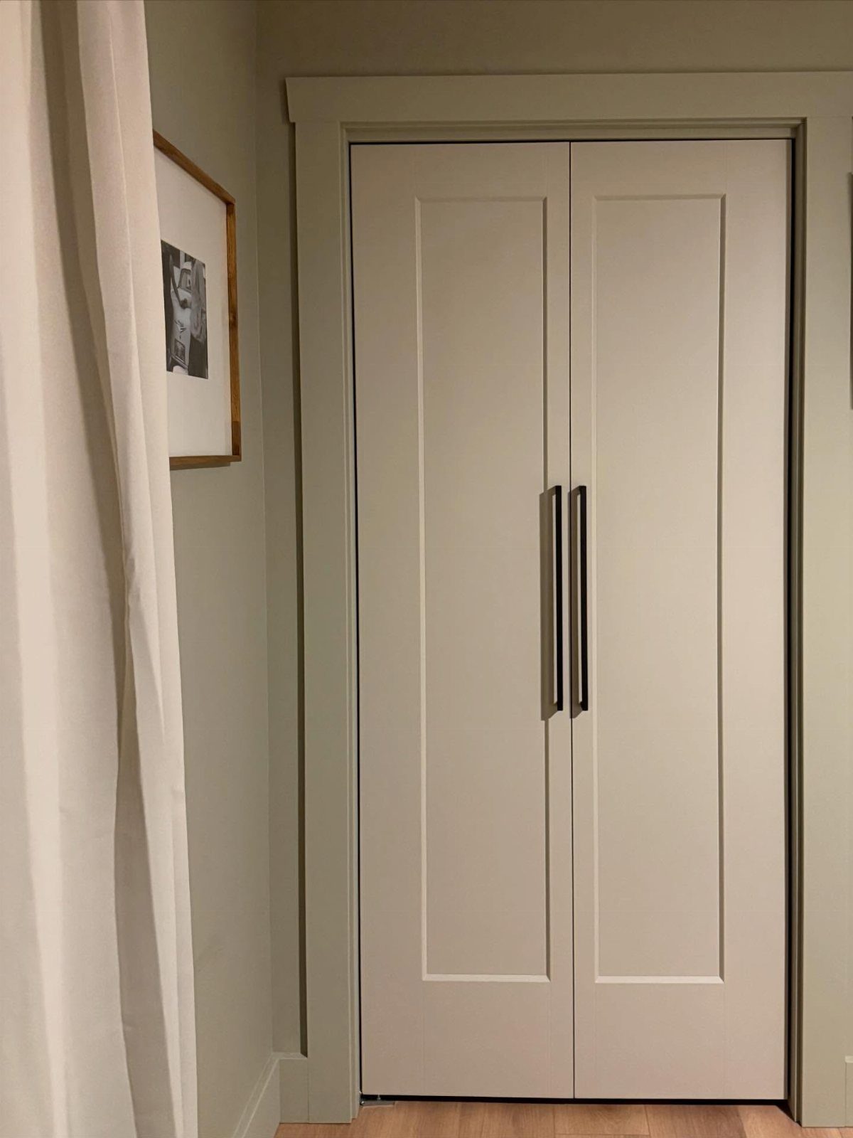White paneled French closet doors with slim vertical black metal pull handles.