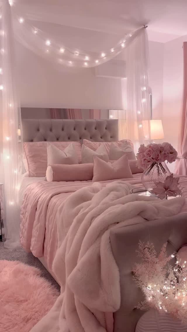 Cozy bed with pink plush bedding, faux-fur throws, and a fairy light canopy.