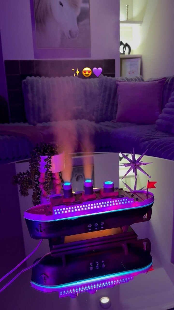 Ship-shaped aromatic diffuser with purple and blue lights emitting mist on a white table