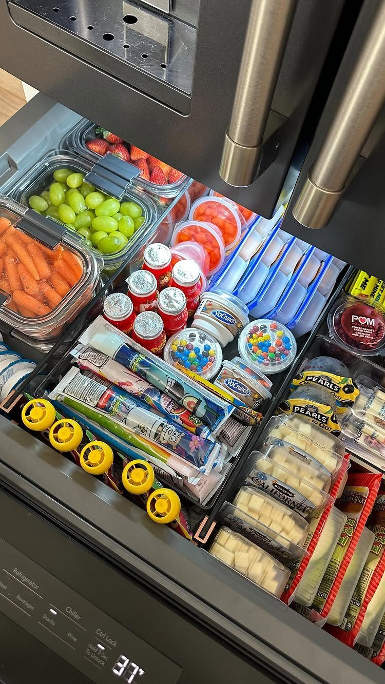 Organized refrigerator drawer containing various pre-portioned snacks in clear plastic bins and containers.