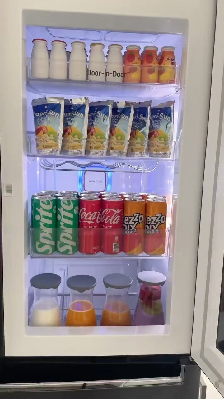 Refrigerator door shelves organized with milk, juice pouches, soda cans, and juice carafes.