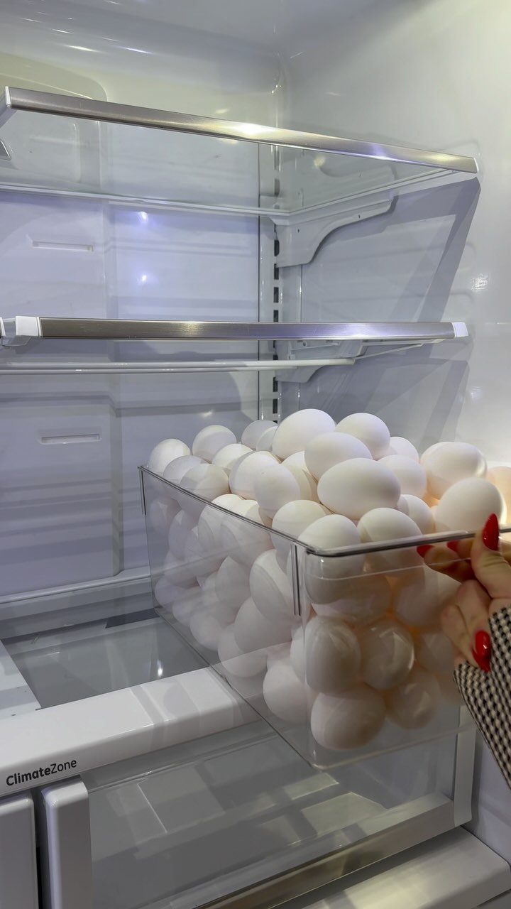 Clear plastic bin filled with white eggs inside a white refrigerator shelf.