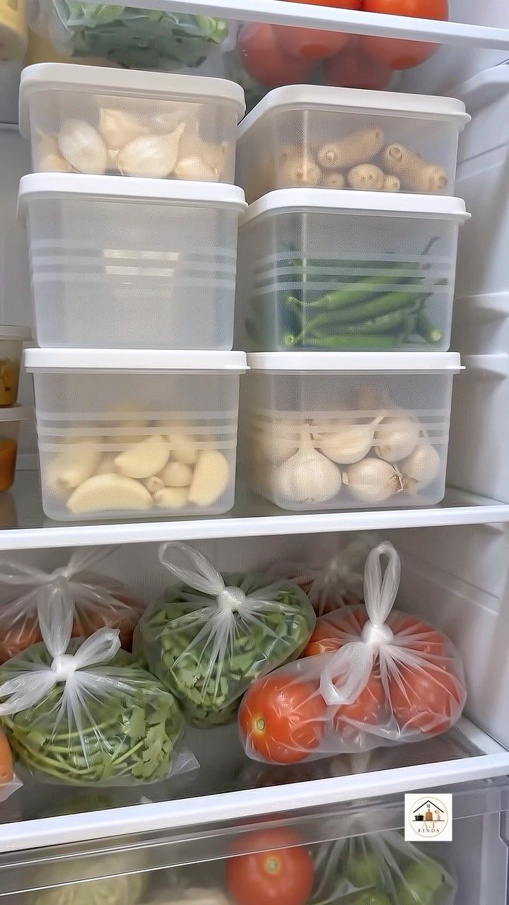 Clear plastic bins and bags organizing vegetables inside a clean white refrigerator.
