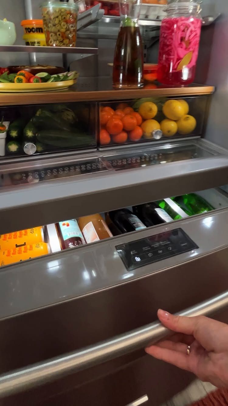 Clear produce drawers in a refrigerator containing cucumbers, tomatoes, and lemons.