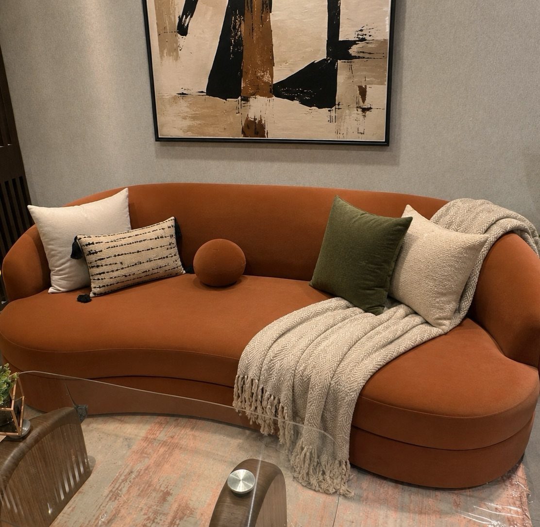 Curved caramel sofa with decorative pillows and a cream knitted throw blanket.