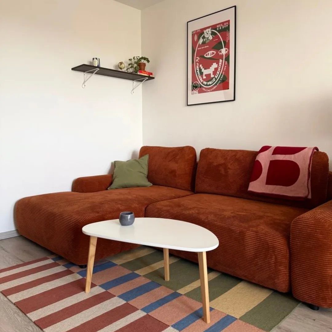Caramel corduroy sectional sofa with a green pillow and white oval coffee table.