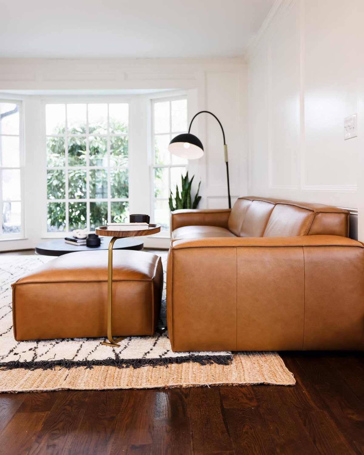 Camel leather sectional sofa and ottoman in a bright modern living room.