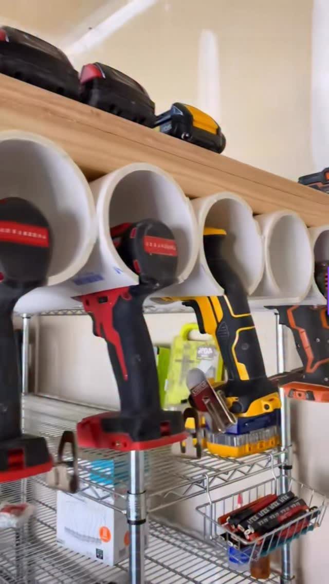 Cordless drills stored upside down in white PVC pipe holders on a wooden shelf.