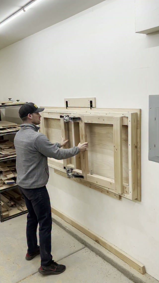 Man operating a wall-mounted folding wooden workbench in a bright workshop setting.