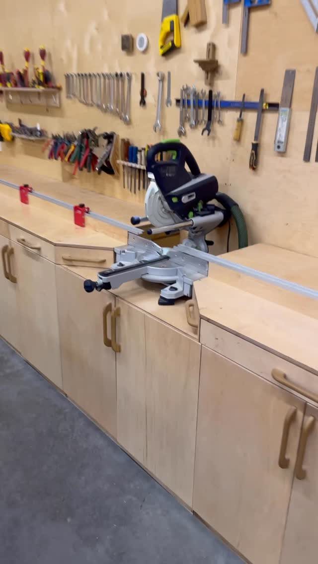 Miter saw built into a wooden workbench with tool storage on the wall