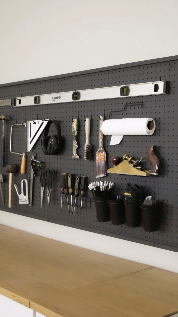 Grey pegboard with organized hand tools and bins above a wooden workbench.