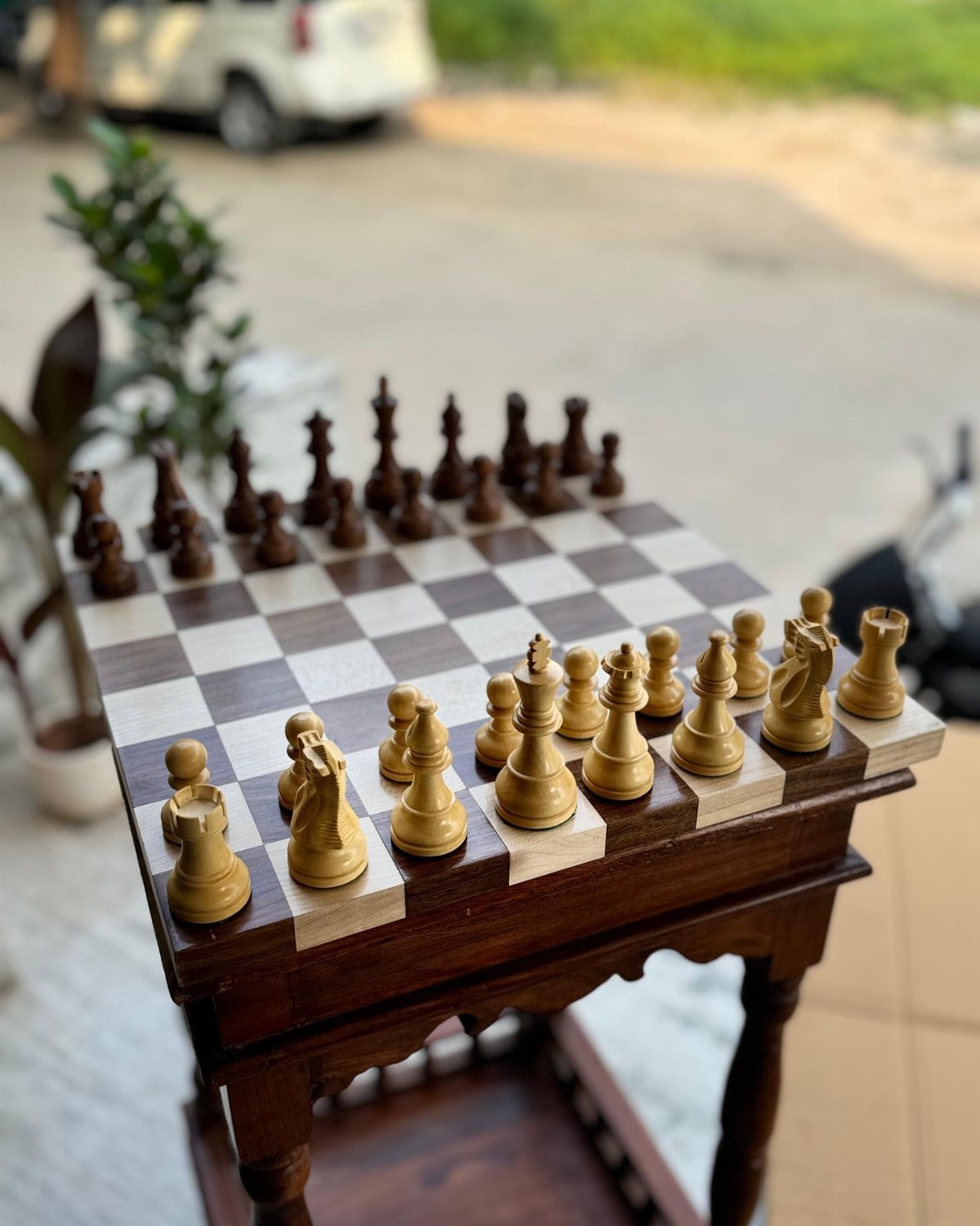 Small wooden chess table with carved pieces set on a light outdoor surface.