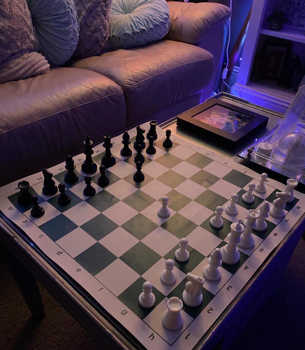 Chess board with pieces on a table next to a tan leather sofa.