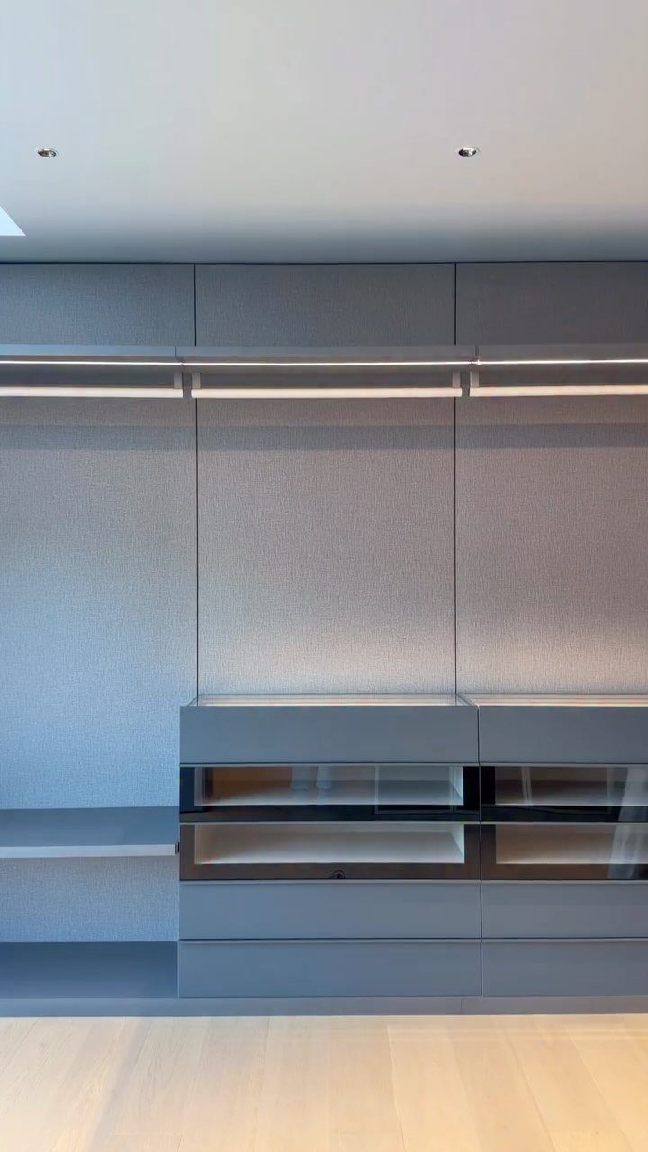 Modern grey built-in closet system with hanging rods and glass-fronted drawers.
