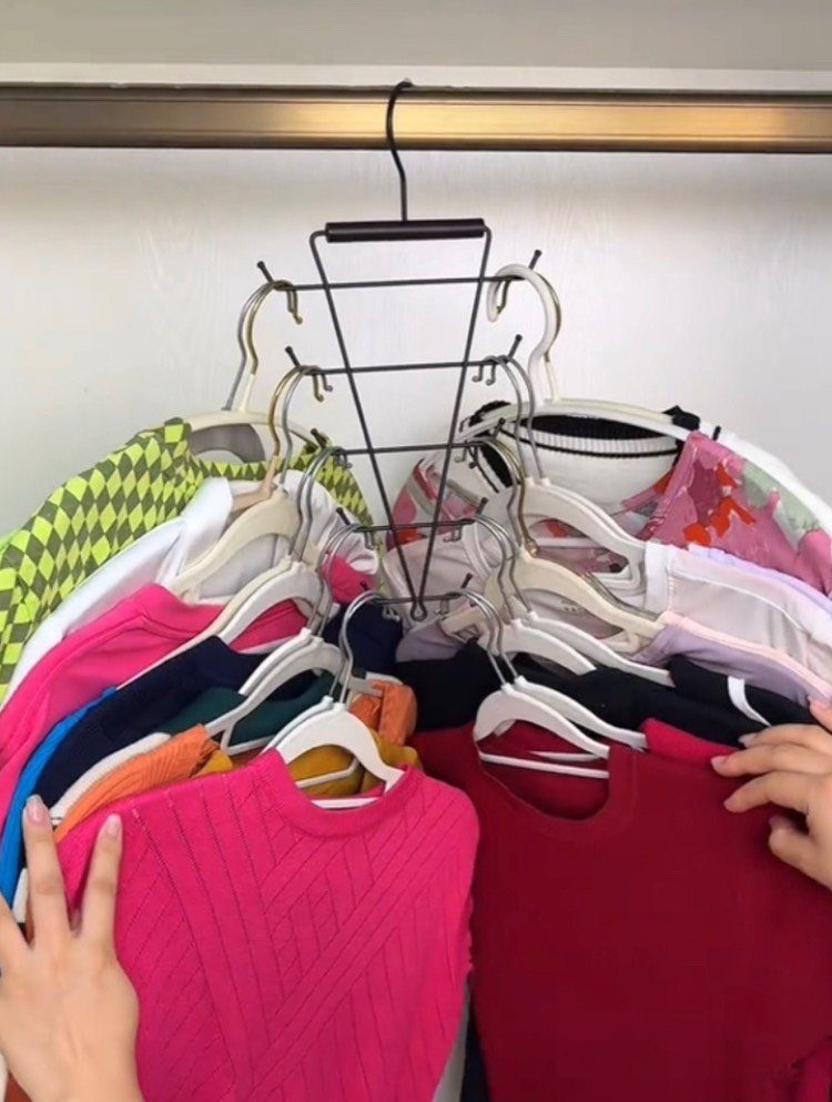 Cascading hanger holding multiple colorful sweaters and shirts on a closet rod.