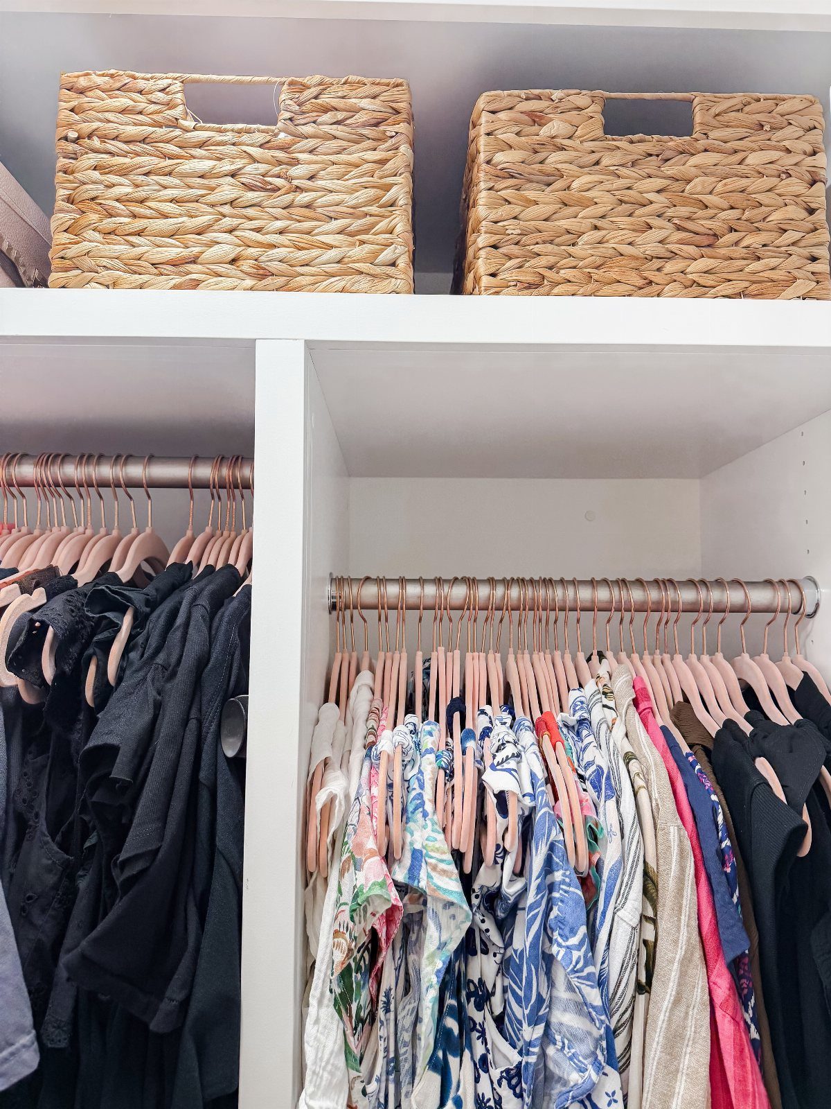 White closet with woven baskets on top shelf and clothes on pink velvet hangers.