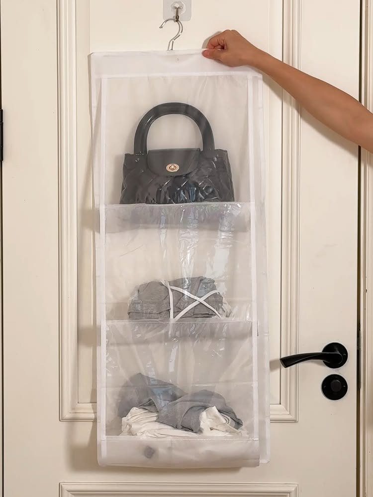 Hanging over-the-door organizer with clear pockets holding a black handbag and folded clothes.