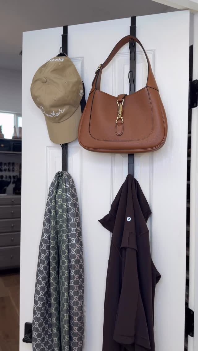 Accessories including a hat, handbag, and scarf hanging on black door hooks.