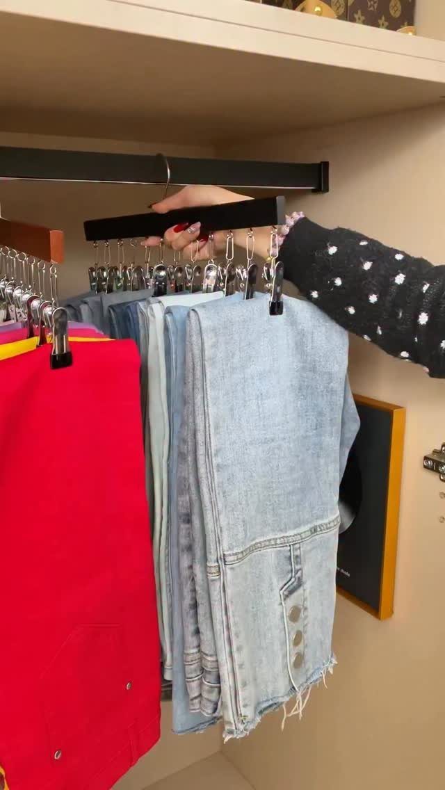 Hand holding a multi-clip hanger with blue jeans and red clothing in a closet.