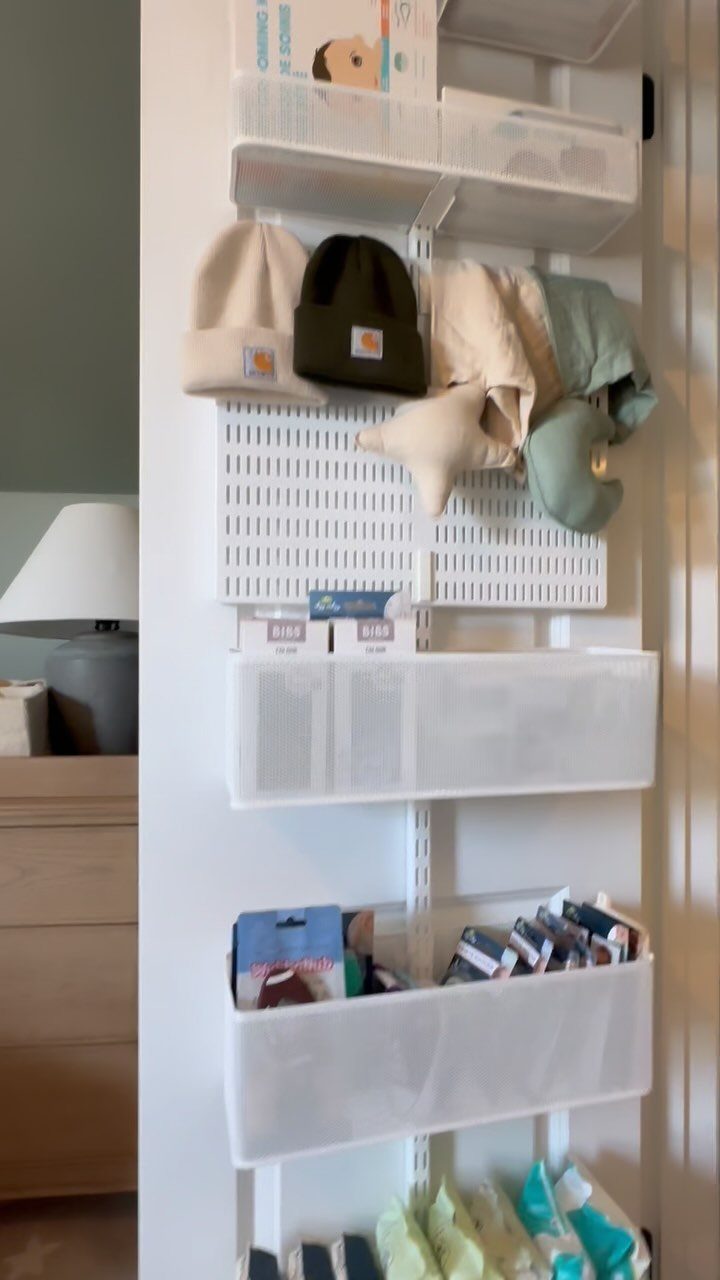 Wall-mounted white storage bins and pegboard holding hats and small organized household items.