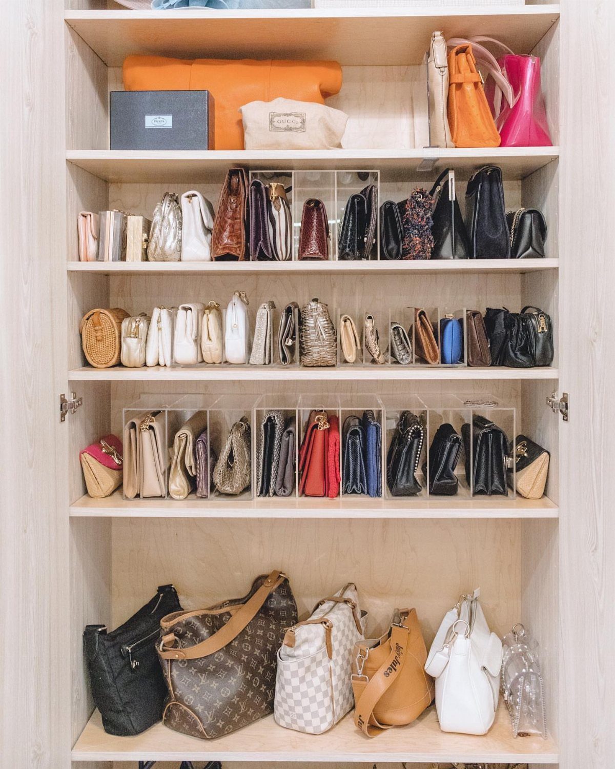 Handbags and purses organized on white closet shelves using clear acrylic dividers.