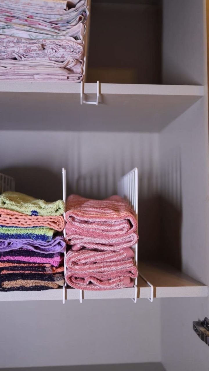 White wire shelf dividers separating stacks of colorful folded towels in a closet.