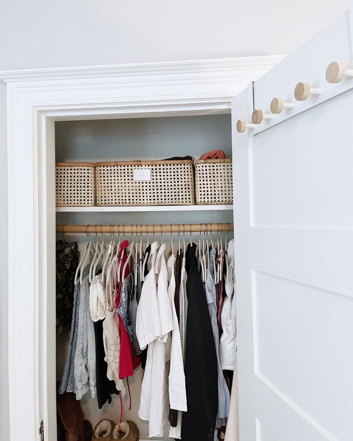 Open white closet with hanging clothes and woven wicker storage baskets on top shelf.